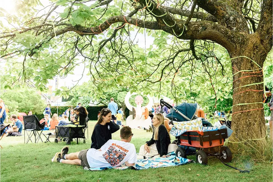 a family are sat on a picnic blanket underneath a tree