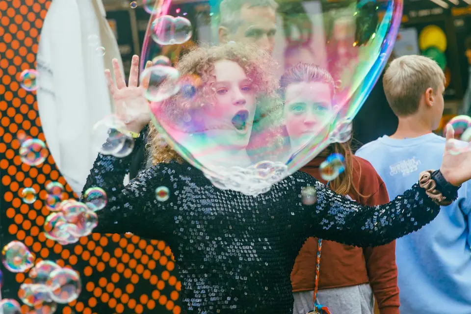 a teenager creates a large bubble with a bubble wand