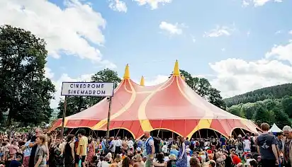 A crowd overspills the yellow and red circus style Cinedrome tent, some groups are sat on the grass.