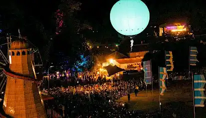 An acrobat attached to a large, blue, floating ballon flies over a huge crowd awaiting the Green Man burn
