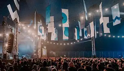 The inside of the Far Out tent, a large crowd of people all facing the stage, hanging from the ceiling are large banners with blue and white symbols.