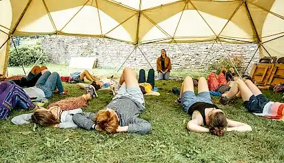 People lie on the grass relaxed during a guided meditation under the canvas of the 'Workshop Dome'