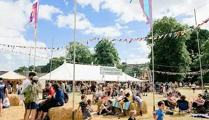 Groups sit on hale bales in the Babbling Tongues area underneath bunting and festival flags