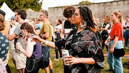 A woman dances with a drink in hand she is wearing sunglasses and is watching a performance