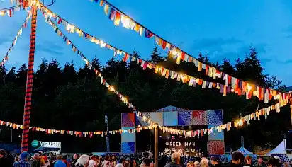 Night-time at the Walled Garden, fairylights and bunting are hung and people gather in front of the Walled Garden stage