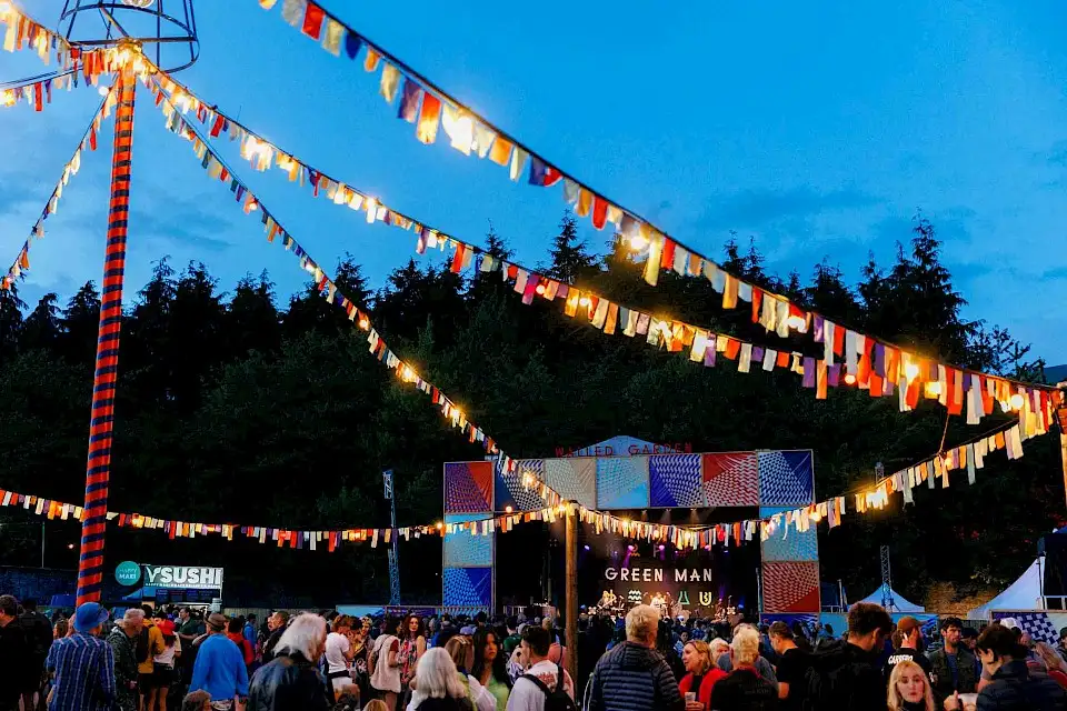Night-time at the Walled Garden, fairylights and bunting are hung and people gather in front of the Walled Garden stage