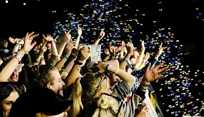 The crowd at the front of the Walled Garden stage, it is night time, their arms are outstretched and there are bubbles everywhere