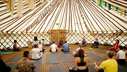 The inside of a large yurt, people are sat cross-legged in a yoga class