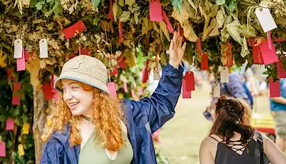 A young girl in a bucket hats puts a paper wish onto the Green Man