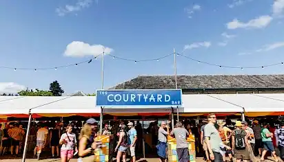 The Courtyard Bar a long white tent with a blue sign above reading 'The Courtyard Bar'