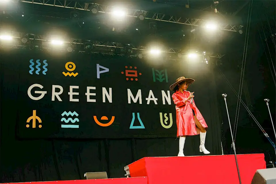 An artist performs on the mountain stage in a large leopard print hat and a long red leather jacket