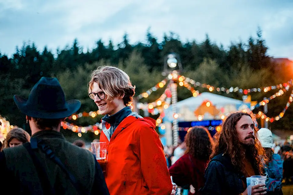 a man in a red coat talks to friends with the walled garden stage in the background