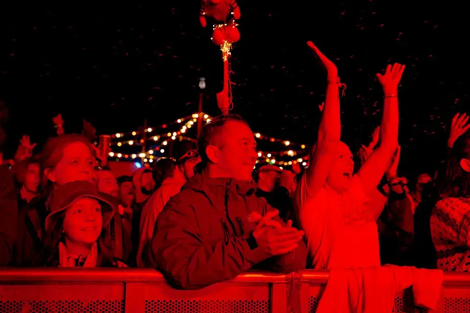 the front row of hte crowd watch a band, they are in a red light, one woman raises her hands to clap