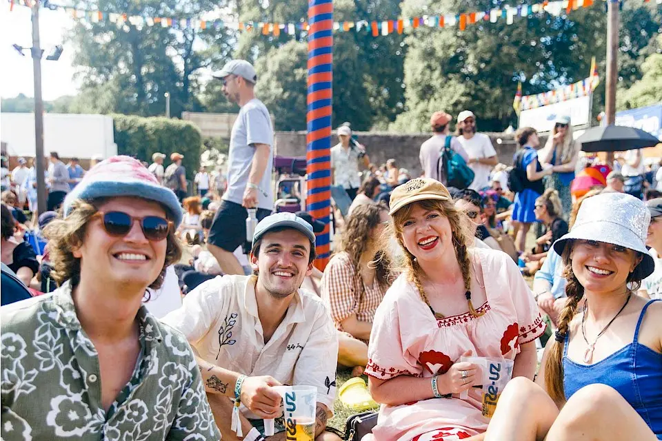 a group of friends smile for the camera, they are sat on the grass in the walled garden