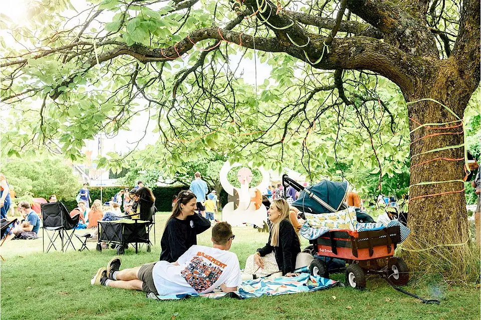 a family are sat on a picnic blanket underneath a tree