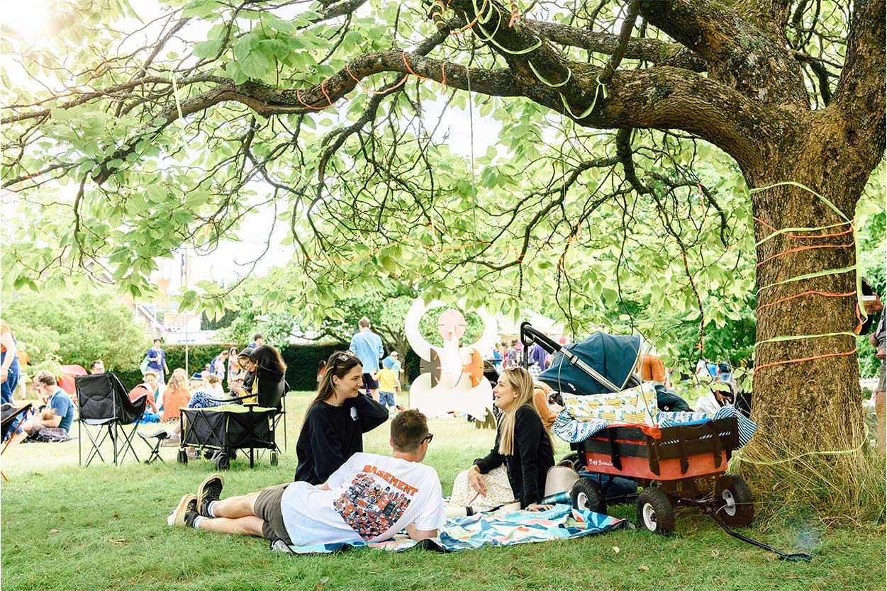 a family are sat on a picnic blanket underneath a tree