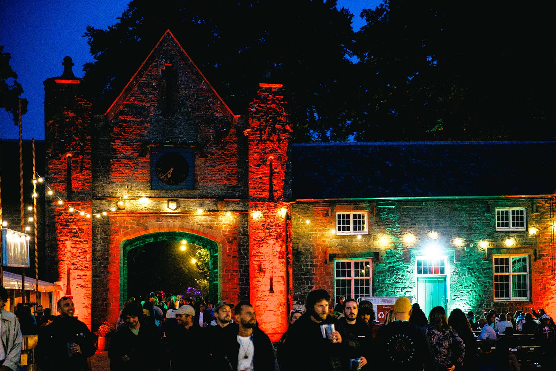 the courtyard at night, the stable buildings are covered with lights and people are gathered