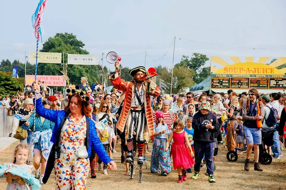 a pirate on stilts and a women in a sparkling jacket lead the little folk parade