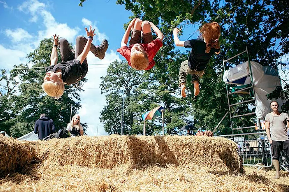 three children backflip off a hay bale