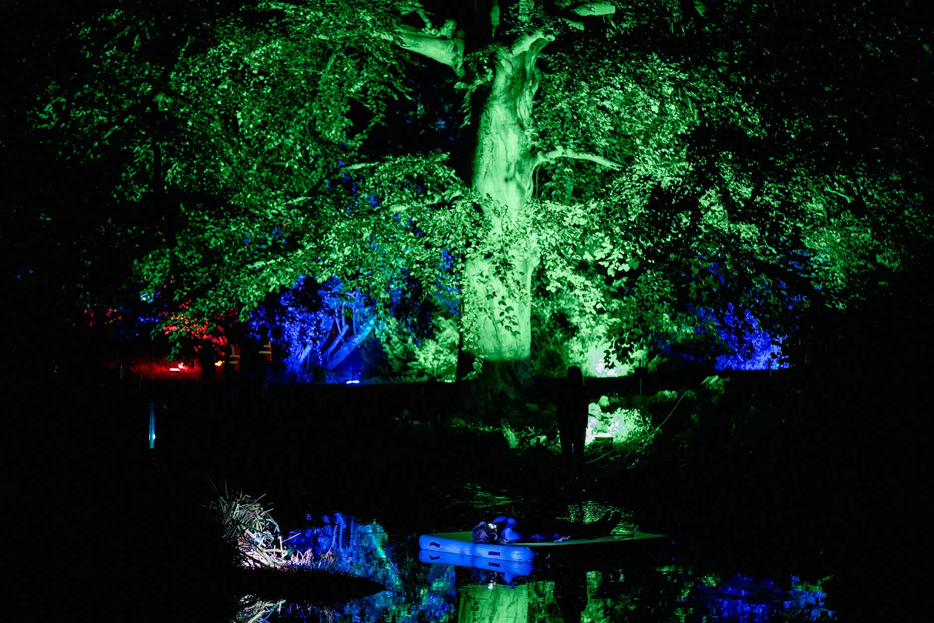 night time an artist is lying on a platform in the middle of the pond