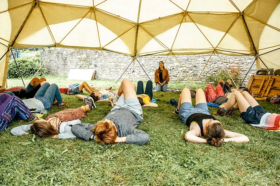 People lie on the grass relaxed during a guided meditation under the canvas of the 'Workshop Dome'