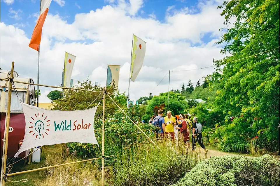 A canvas sign for WildSolar, there are festival flags and trees surrounding it