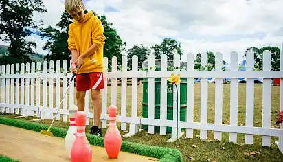 A boy is playing minigolf, there are bowling pins on the course