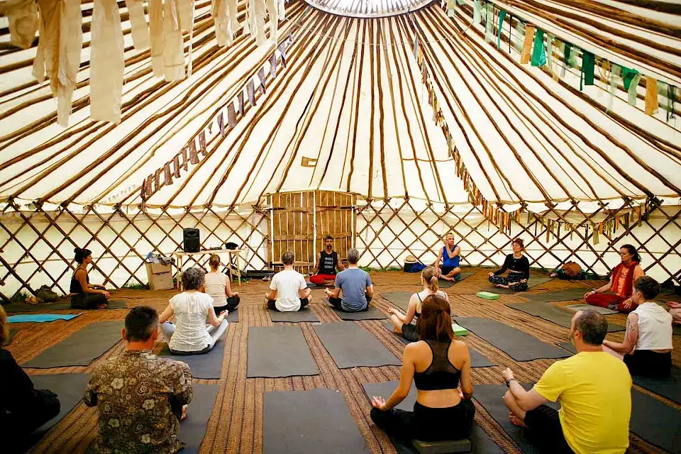 The inside of a large yurt, people are sat cross-legged in a yoga class