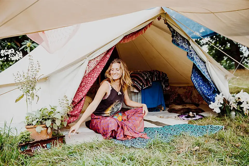 A woman sits outside her tent with plants