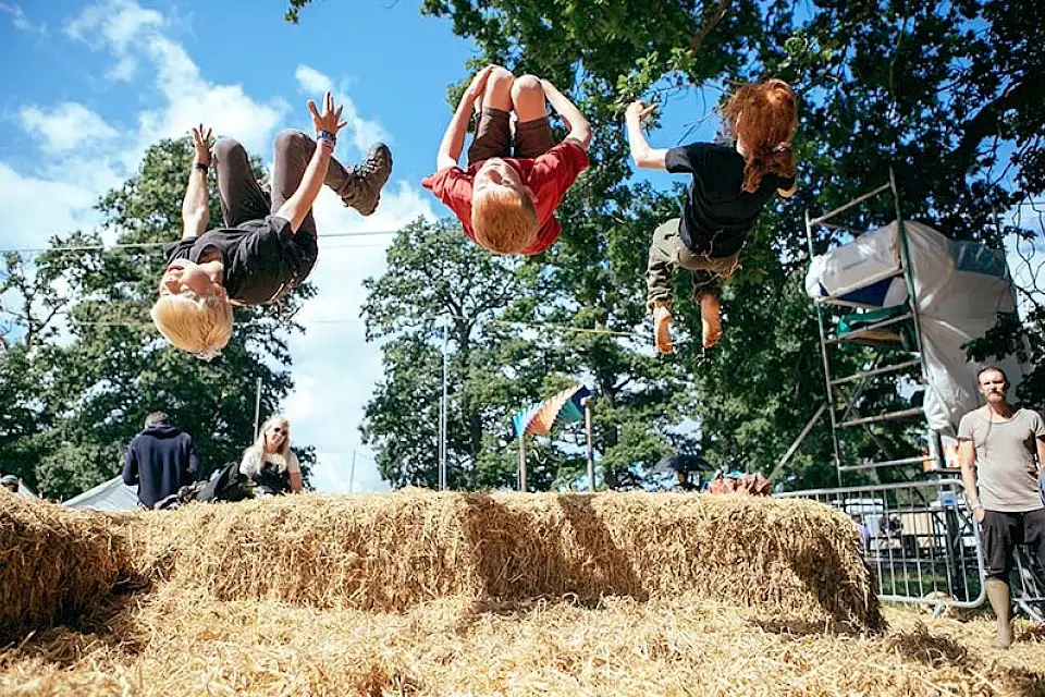 Three children backflip off a hay bale