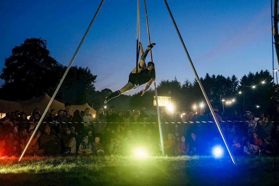 A trapeze artist performs at dusk with a crowd onlooking