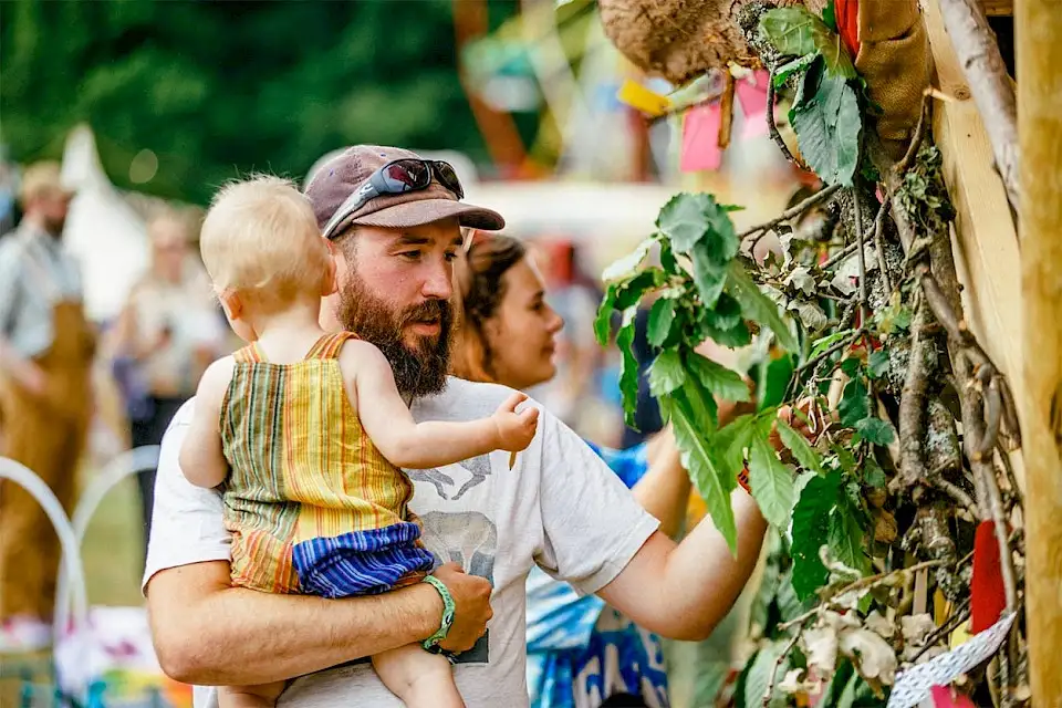 A man holding a baby explores the Green Man sculpture
