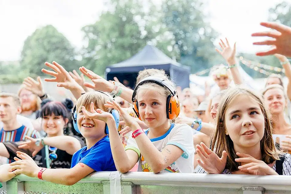 Children with eardefenders on at the barrier of the stage wave their hands