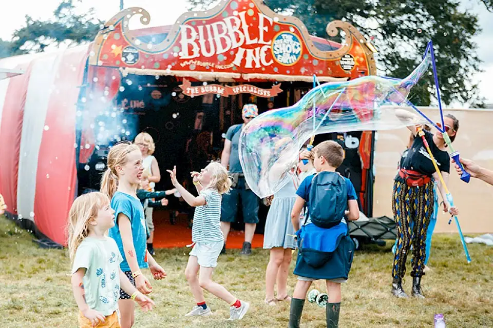 Children play infront of the 'Bubble Inc.' stall, there are giant bubbles being made
