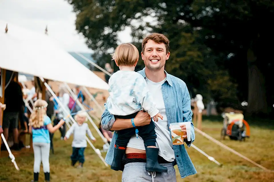 A man carrying a toddler smiles at the camera
