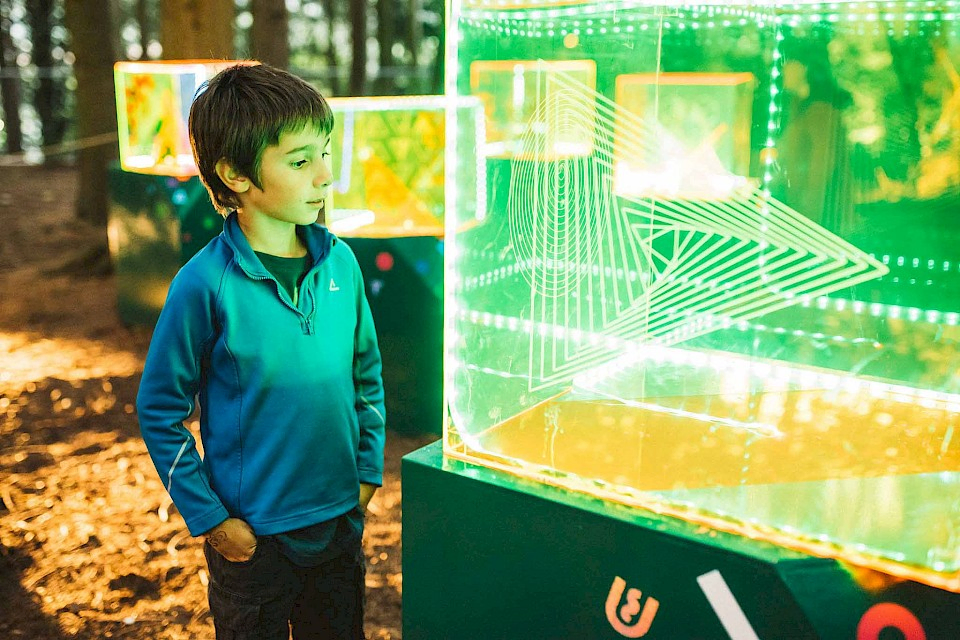 A boy looks at an arts installation of a box of green lasers